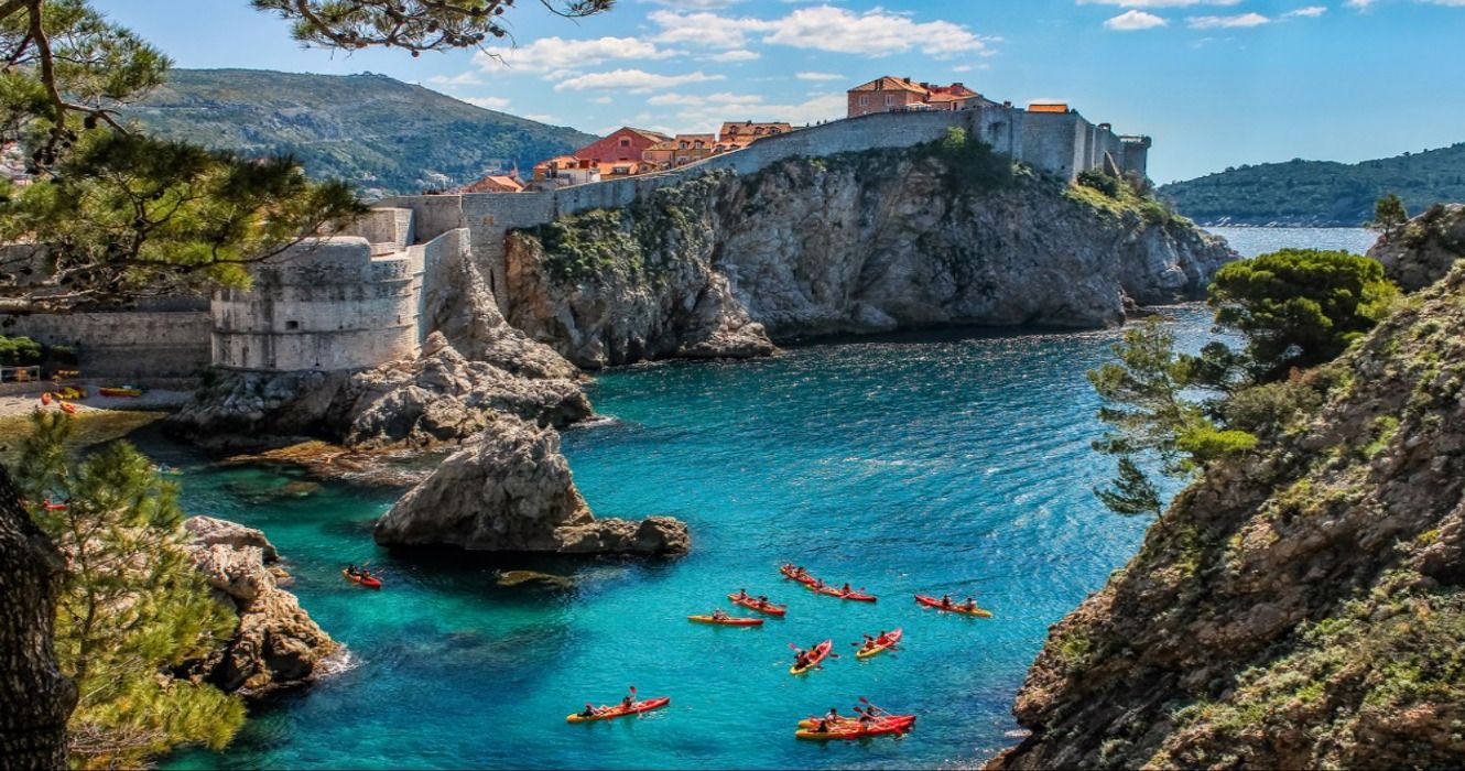 Dubrovnik West Harbor and its ancient city walls as people kayak in the sea, Croatia
