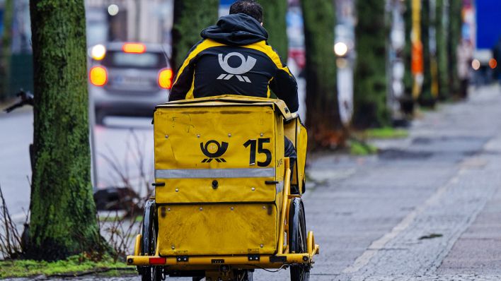 Symbolbild:Ein Briefträger fährt mit seinem Fahrrad eine Straße entlang.(Quelle:picture alliance/dpa/M.Skolimowska)