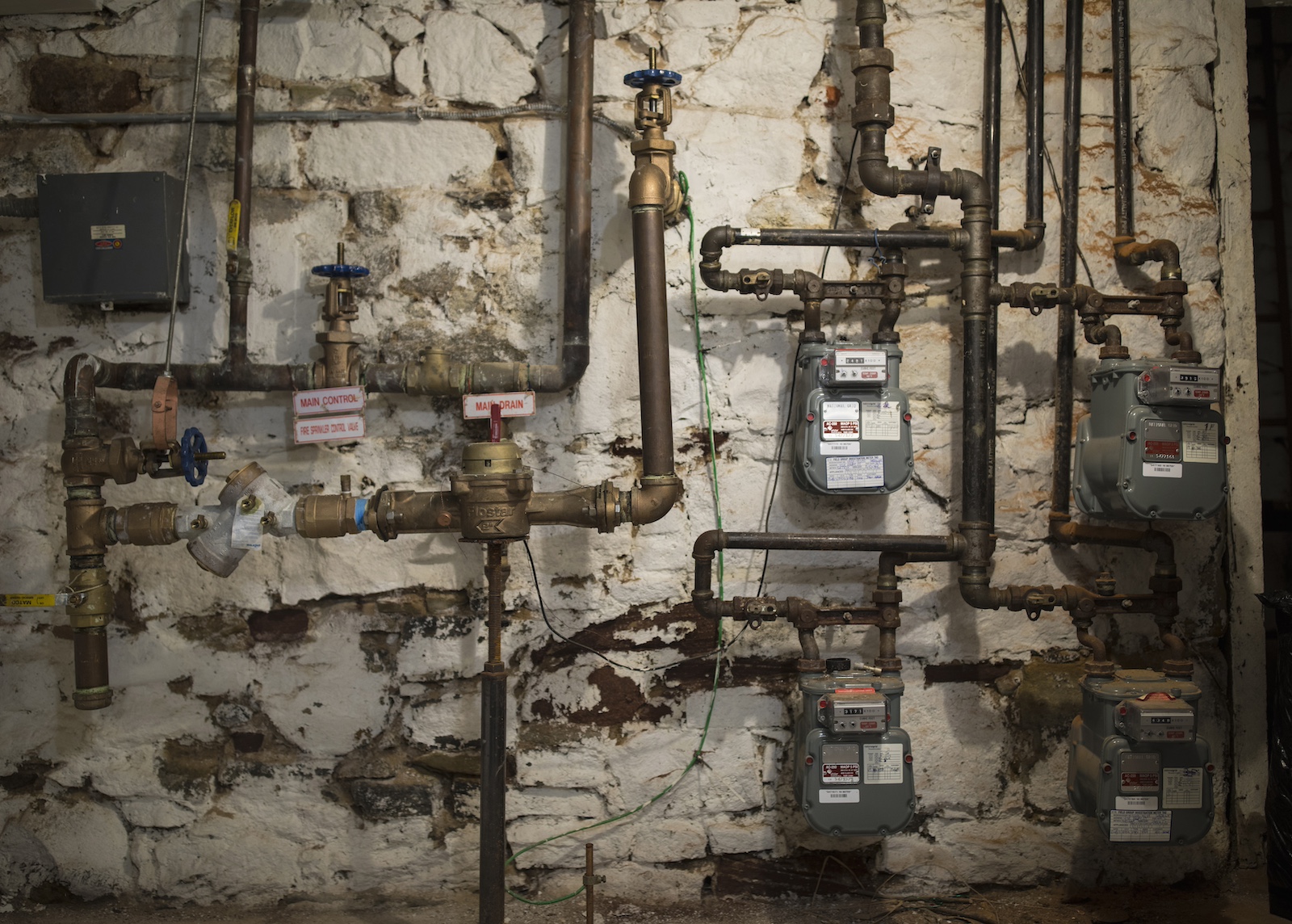 A gray wall with a thick maze of pipes running horizontally and vertically in front of it