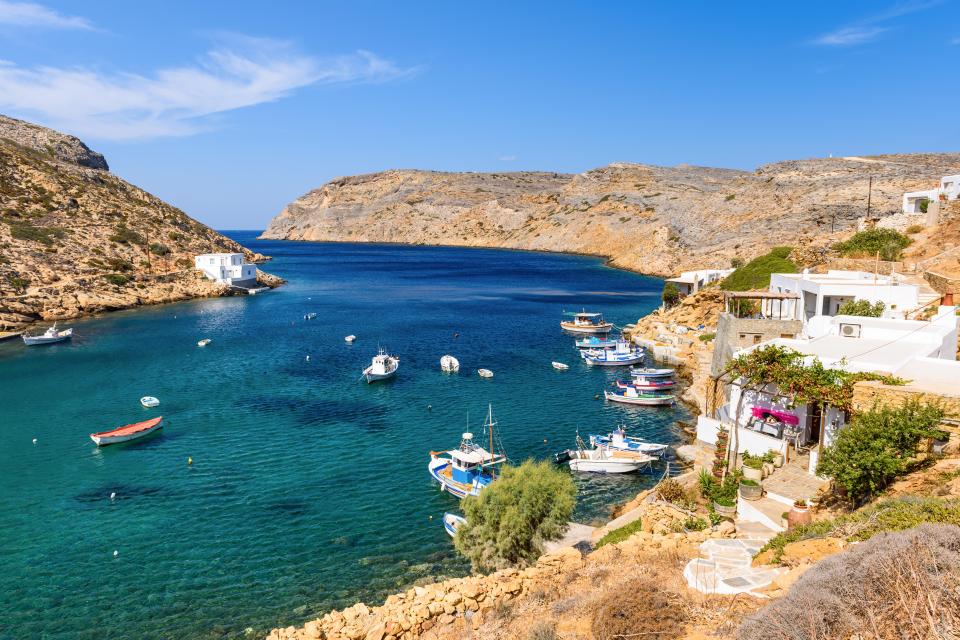 Boats in a sheltered bay near white houses on the coast of Sifnos, Greece.