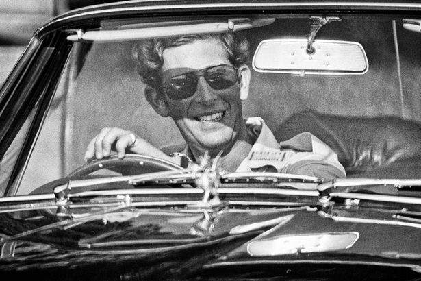 01/01/1975: Charles, then Prince of Wales pictured wearing sunglasses, smiling at the wheel of his Aston Martin sports car at the Windsor, England polo grounds