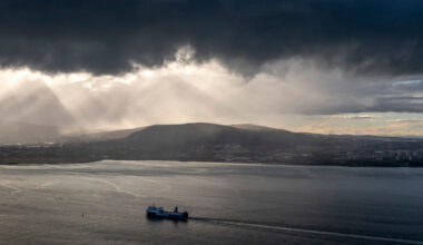 Heavy cloud hangs over Belfast Lough where a ferry is sailing towards Belfast Harbour. Belfast, Northern Ireland.