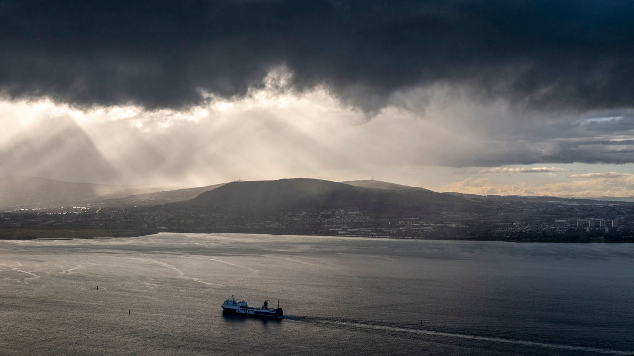 Heavy cloud hangs over Belfast Lough where a ferry is sailing towards Belfast Harbour. Belfast, Northern Ireland.