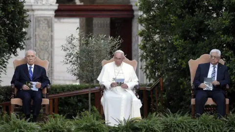 Reuters Pope Francis, Shimon Peres and Mahmoud Abbas. Pope Francis is in a garden with the two politicians flanking him. They are all seated.