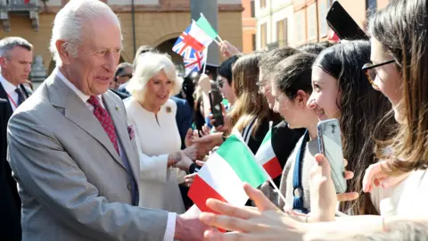Reuters King Charles and Queen Camilla visit a market in the Piazza del Popolo, greeting young women in in the street