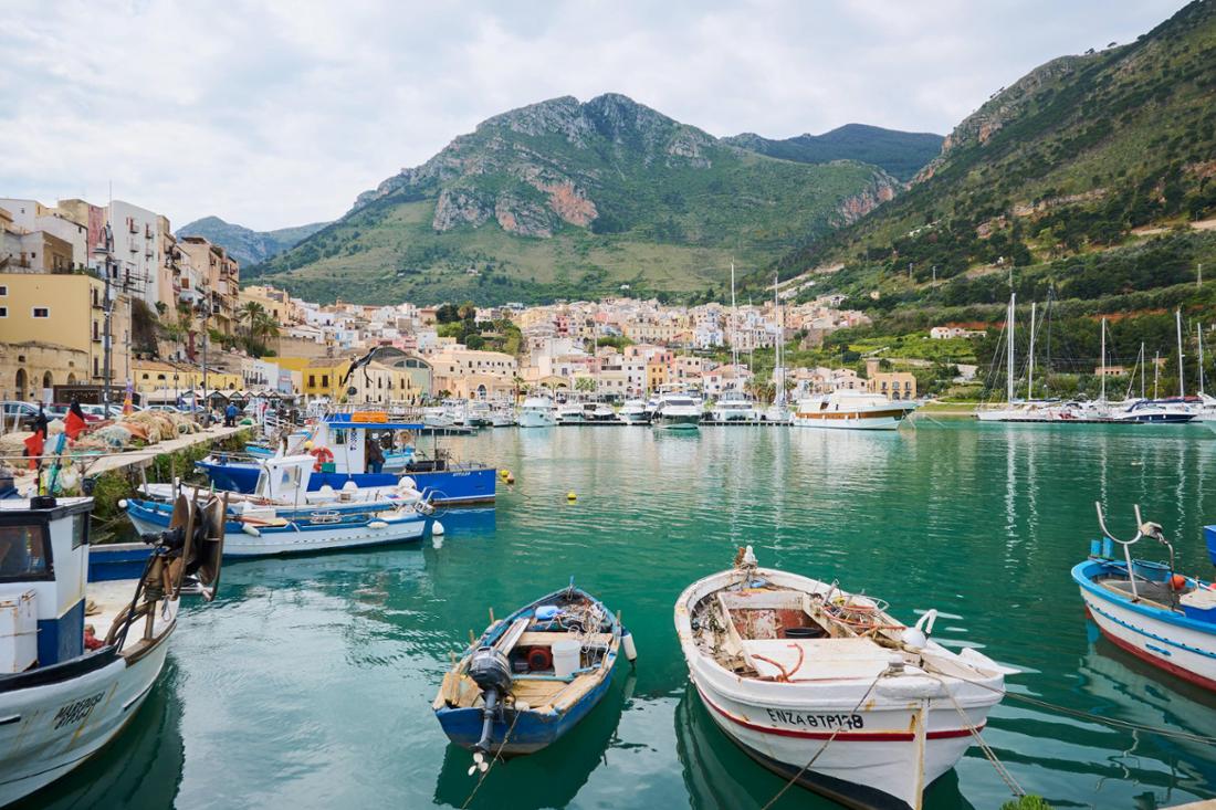 Im Hafen von Castellammare del Golfo auf Sizilien liegen Fischerboote vor Anker, umgeben von bunten Gebäuden.