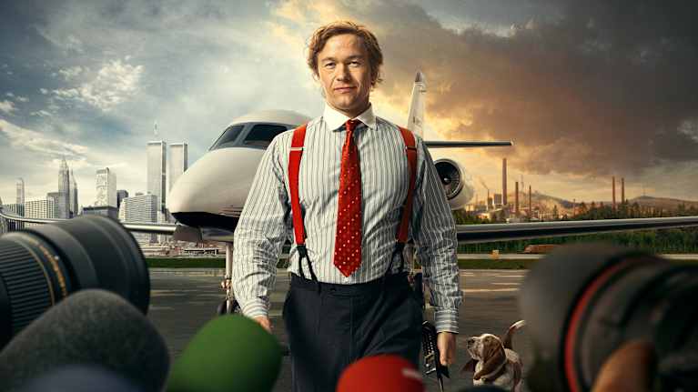 Jan Stenbeck (Jakob Oftebro) kommer gående mot mickar och kameraobjektiv, i bakgrunden syns ett privatflygplan och skyskrapor.