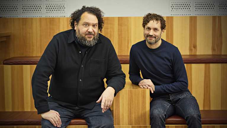 Regissören Goran Kapetanović och manusförfattaren Alex Haridi sitter bredvid varandra och ser rakt in i kameran och ler.