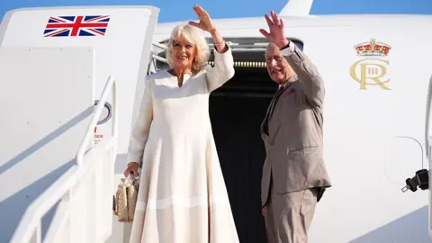 PA Media King Charles III, wearing a grey suit, and Queen Camilla, wearing a white dress and carrying a handbag, wave as they depart from Forli Airport as they leave Italy on the last day of the four day state