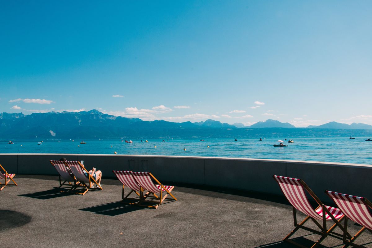 Chaises longues sur une promenade face au lac Léman avec vue sur les montagnes en arrière-plan par une journée ensoleillée. Chaises longues sur une promenade face au lac Léman avec vue sur les montagnes en arrière-plan par une journée ensoleillée.