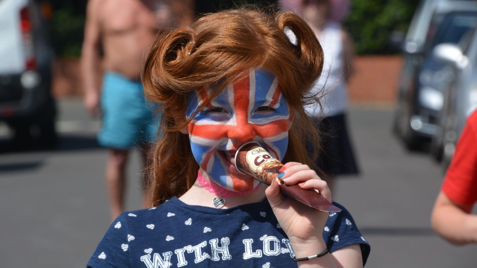 Girl with Union Jack face paint eating ice cream at a street party.