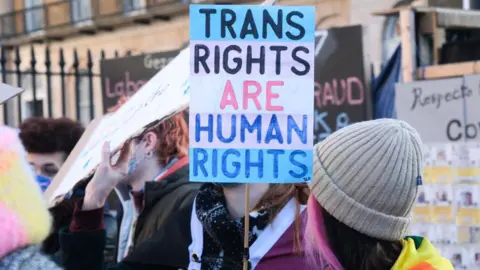 Getty Images Trans rights protesters during a march. One is holding a placard which says Trans Rights Are Human Rights