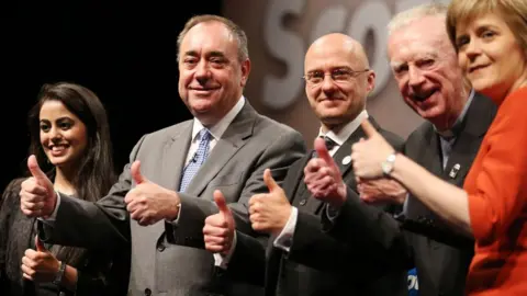 PA Media Five people, two women at either end with three men in the middle, pose with their thumbs up while standing in a line. 
