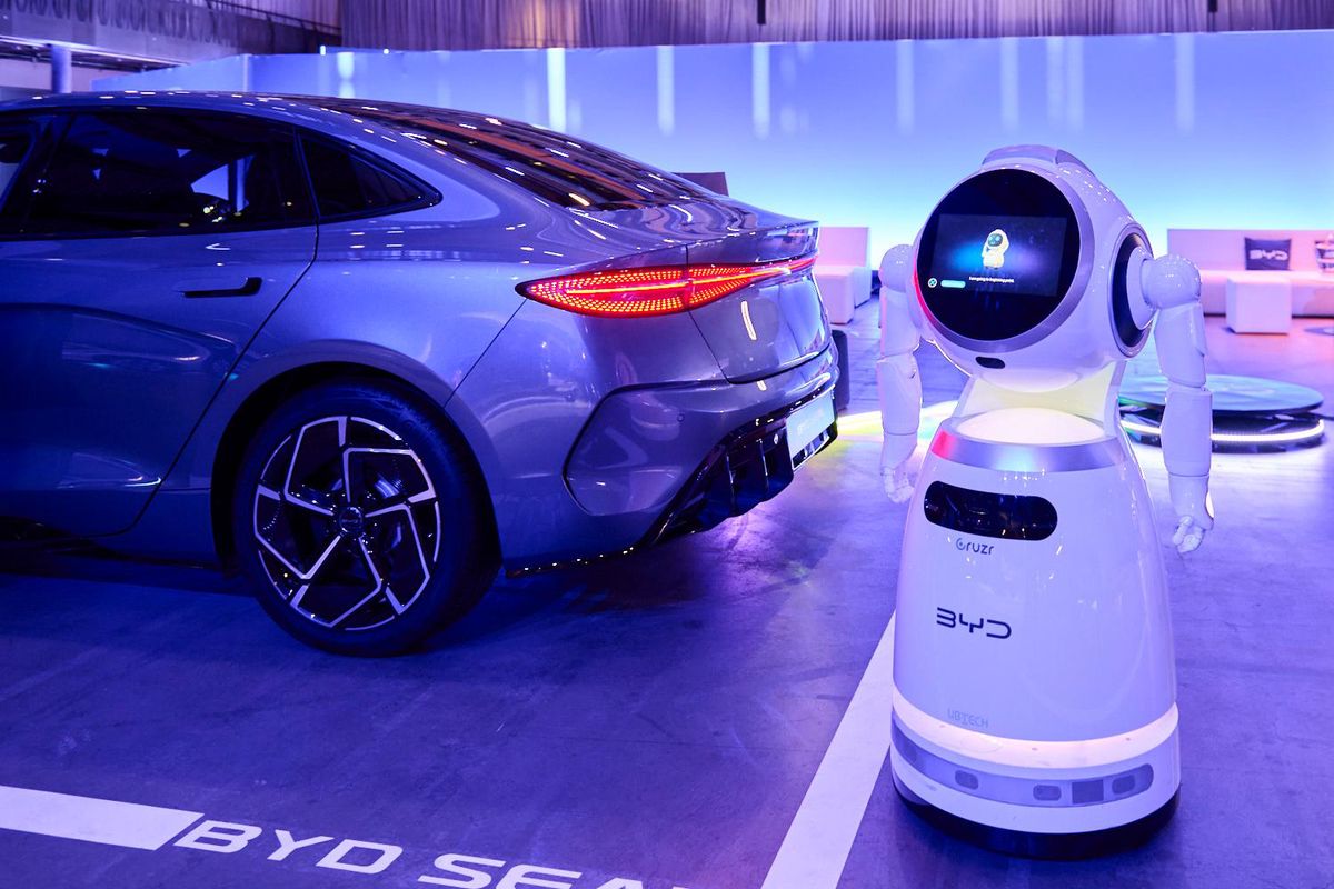 Ein BYD-Elektroauto in einer Ausstellungsumgebung neben einem BYD-Roboter stehend. Das Auto hat ein modernes Design und ist in einem Ausstellungssaal beleuchtet.