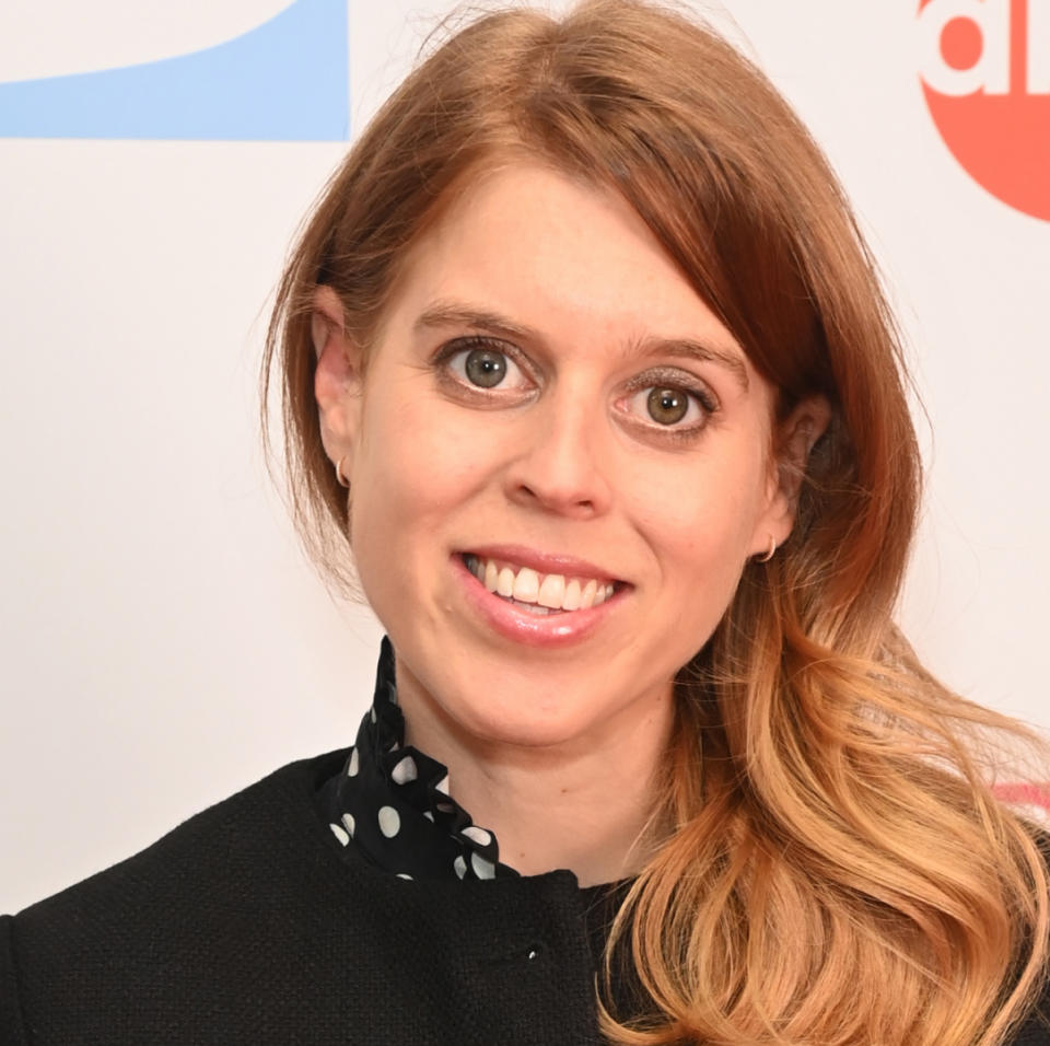 Princess Beatrice wearing a black jacket and polka dot dress smiling at the camera .