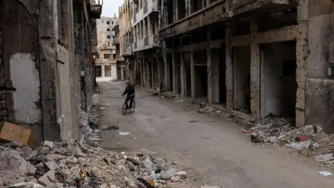 Getty Images A boy on a bicycle cycles between two building which are in ruins