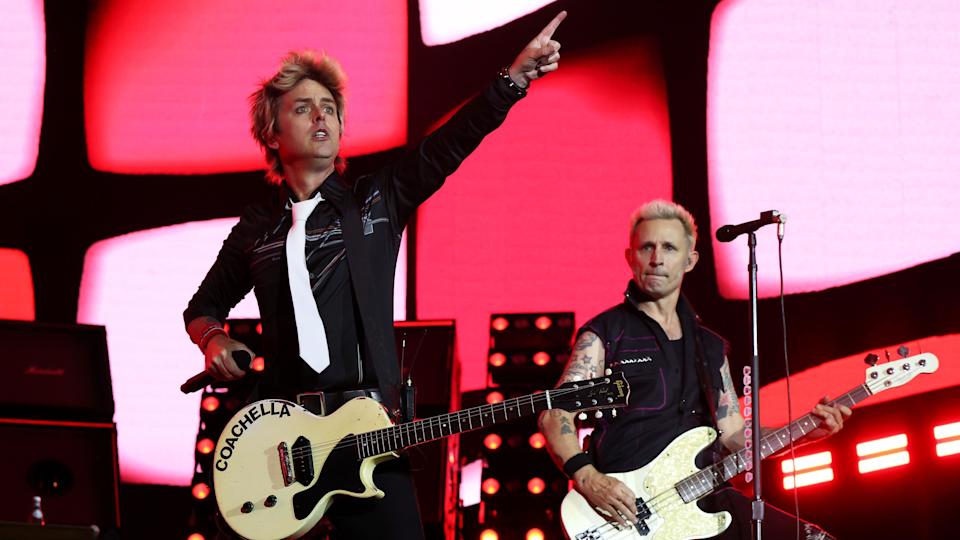 Green Day's Billie Joe Armstrong and Mike Dirnt perform at Coachella, wearing black with red lights behind them.
