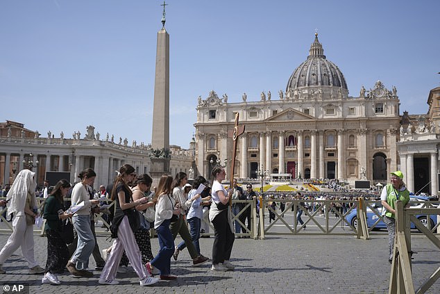 Pilgrims, one holding a cross, walk in St. Peter's Square at the Vatican after Cardinal Camerlengo Kevin Joseph Farrell announced the death of Pope Francis today
