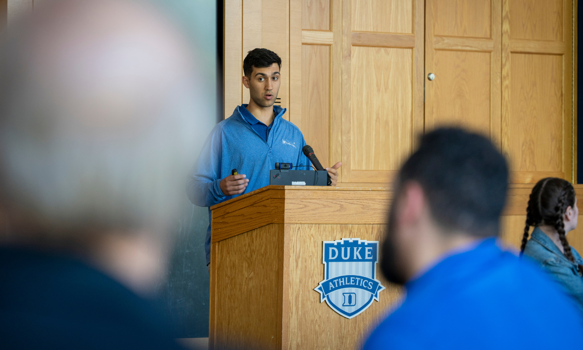 A young man standing at a podium speaks to an audience.