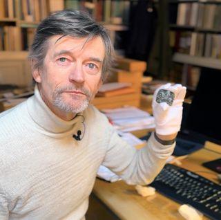 a man sitting at a desk holds up a small metal stamp
