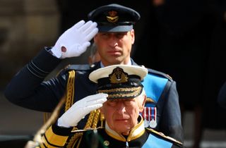 King Charles and Prince William wearing military uniforms and saluting at Queen Elizabeth's funeral in 2022