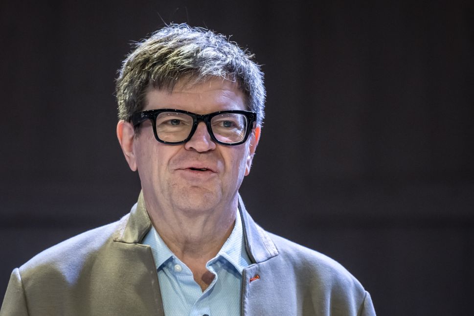 Man in black glasses and grey blazer pictured against dark background