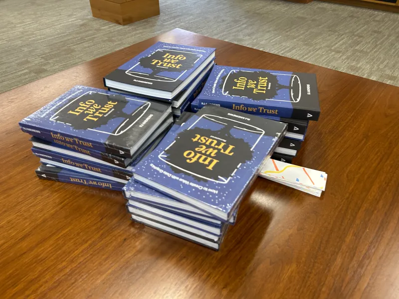 4 stacks of books on a wooden table.