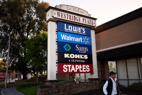 A person walks past a cluster of retail store signs in La Habra, Calif., Wednesday, April 2, 2025. (AP Photo/Jae C. Hong)