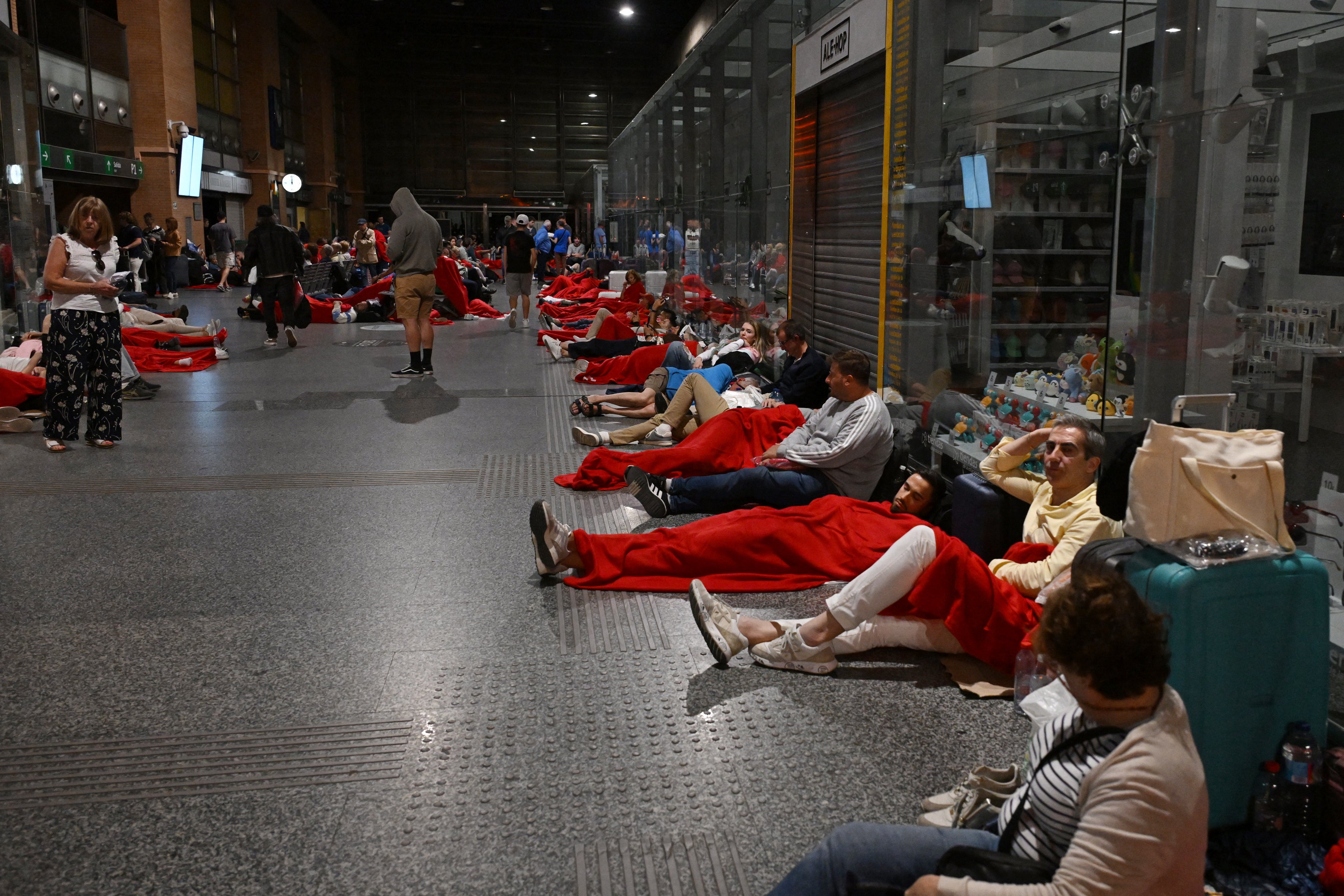 Travelers covered with Red Cross blankets lie on the floor, as they prepare to spend the night at the Cordoba train station, following a massive power cut affecting the entire Iberian peninsula and the south of France