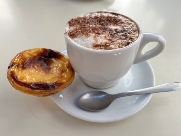 a pastel de nata tart next to a cappuccino
