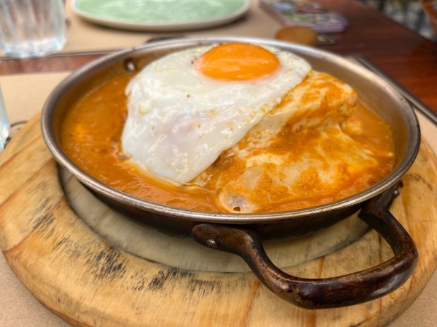 A smothered sandwich topped with a sunny-side-up egg