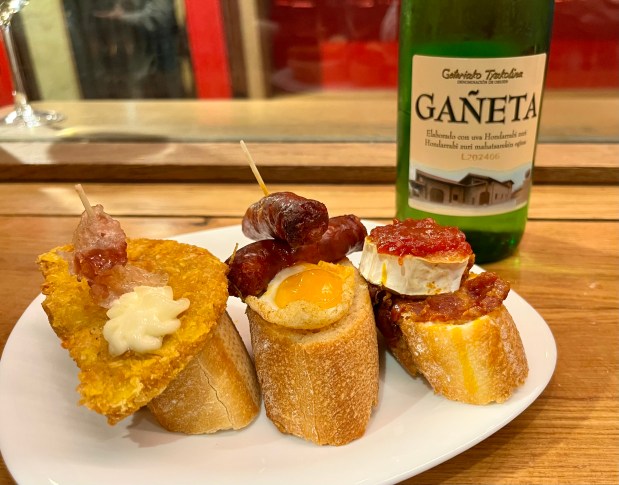 Three baguette slices topped with, from left, a potato cake, sausages and a quail egg, and brie cheese with jam
