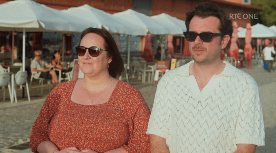 A man and a woman walking outdoors, wearing sunglasses.