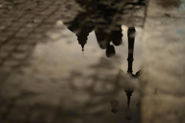 People and the St. Peter's Basilica are reflected in a puddle