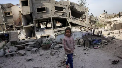 AFP A Palestinian girl walks past a destroyed building following overnight Israeli strikes on Jabalia's south-western district of Nazla, in northern Gaza (16 April 2025)