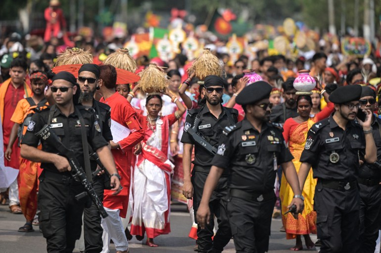 Security personnel stand guard as people march down a street during celebrations marking Bengali New Year in Dhaka on April 14, 2025. (Photo by MUNIR UZ ZAMAN / AFP)