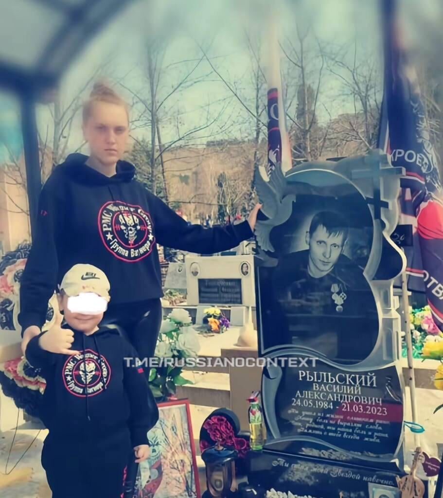 Child of a dead Wagner soldier standing happily next to his fathers grave