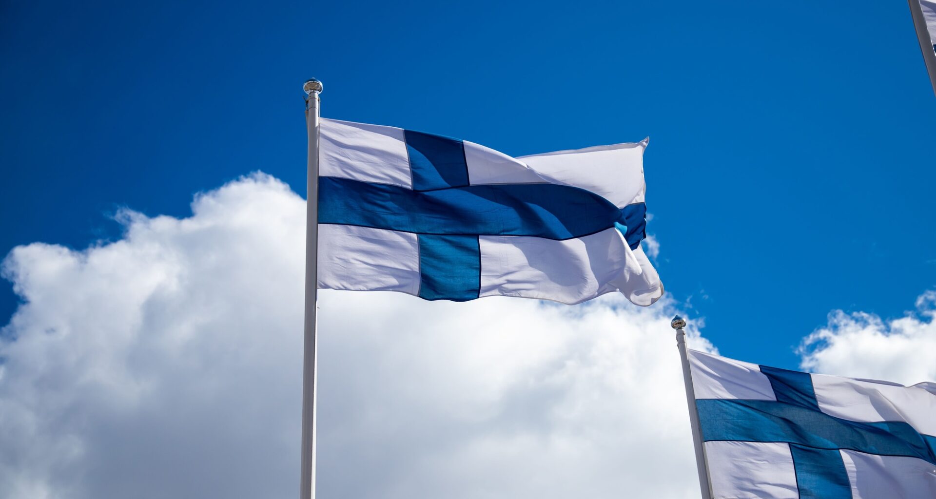Finland flags waving on a flag pole in background of cloudy sky