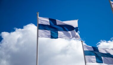 Finland flags waving on a flag pole in background of cloudy sky