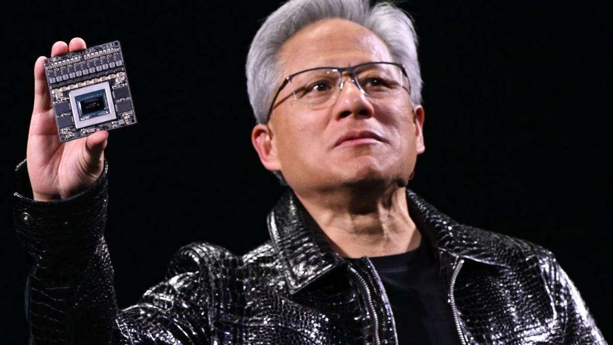 Nvidia CEO Jensen Huang, wearing a shiny black jacket, holds one of the company&apos;s computer chips.