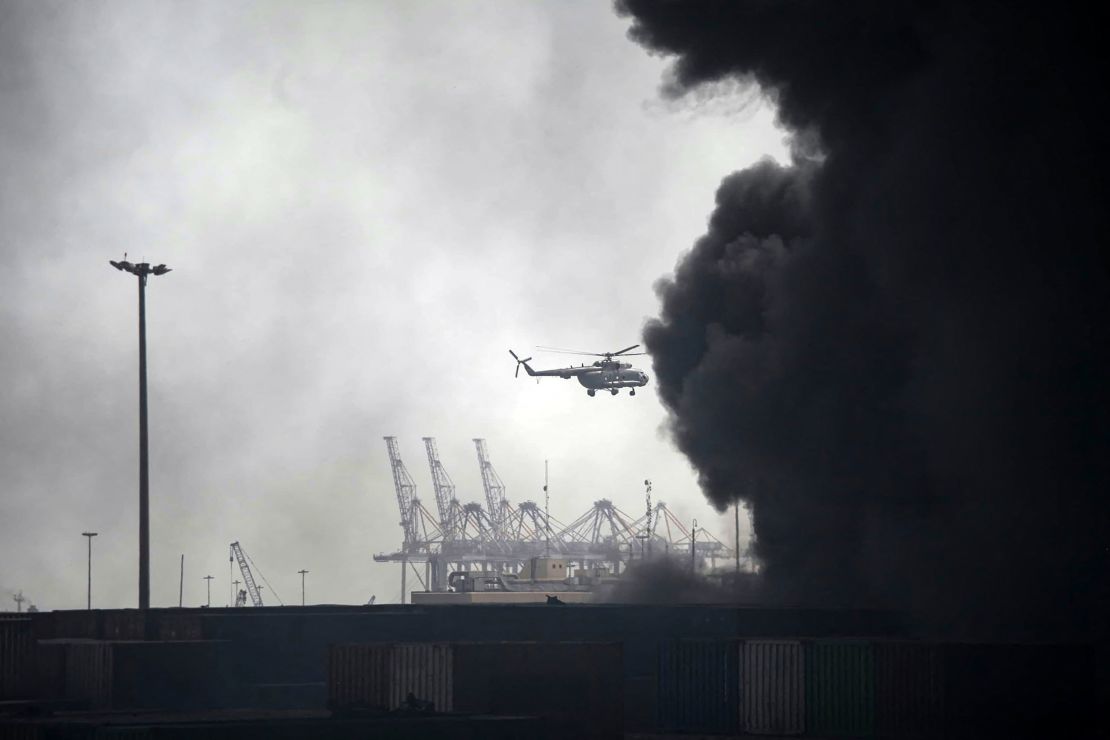 A helicopter flies through black smoke engulfing the site of a port blast in Iran, on Saturday, which killed at least five people and injured more than 700 others.