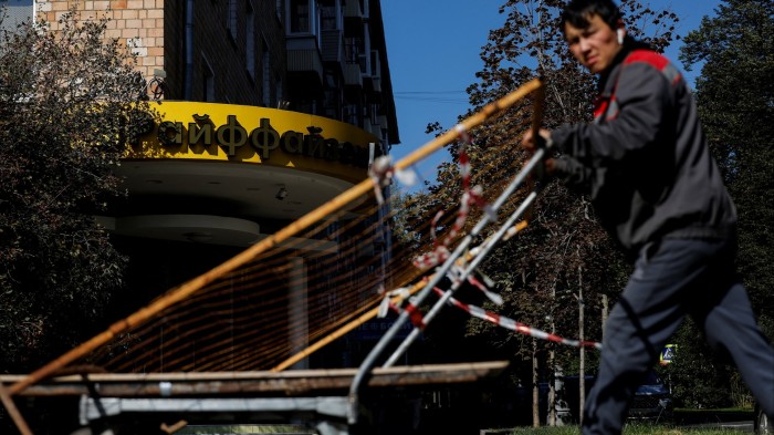 A worker pushes a cart past the entrance of a Raiffeisen Bank branch in Moscow, Russia
