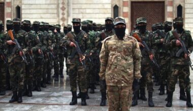 The soldiers are lined up and are wearing balaclavas and carrying rifles