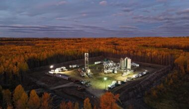 Oil or gas drilling site brightly lit in a clearing, surrounded by dense autumn forest with orange foliage