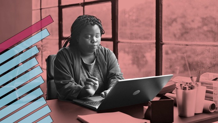 Woman with braided hair working on a laptop at a desk by large rain-speckled windows