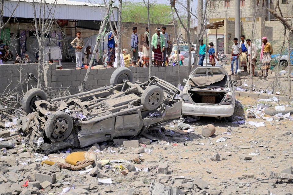 Damaged cars and bystanders in a war zone.