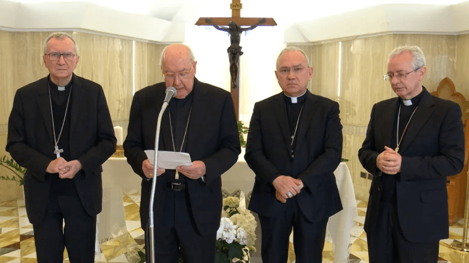 Four bishops standing in a chapel, one reading from a paper.