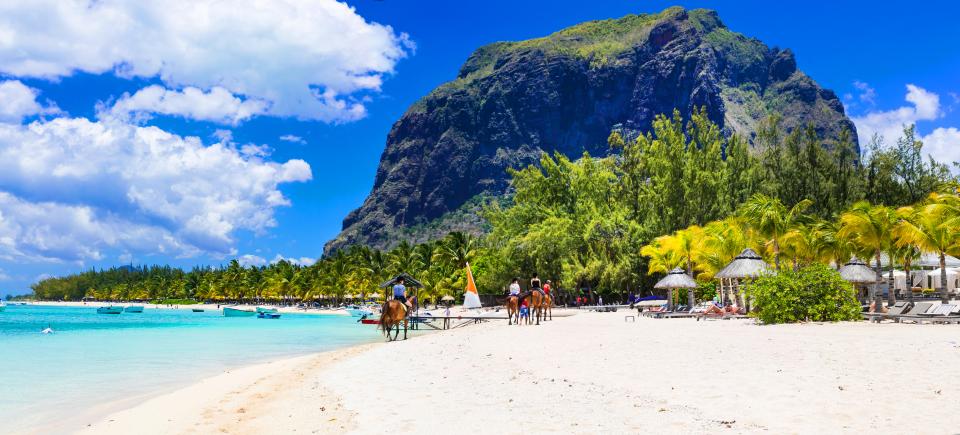 Beach scene in Mauritius with people horseback riding on the sand.