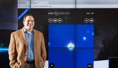 Photo of a man standing next to a large projected image of the Disk Detective website