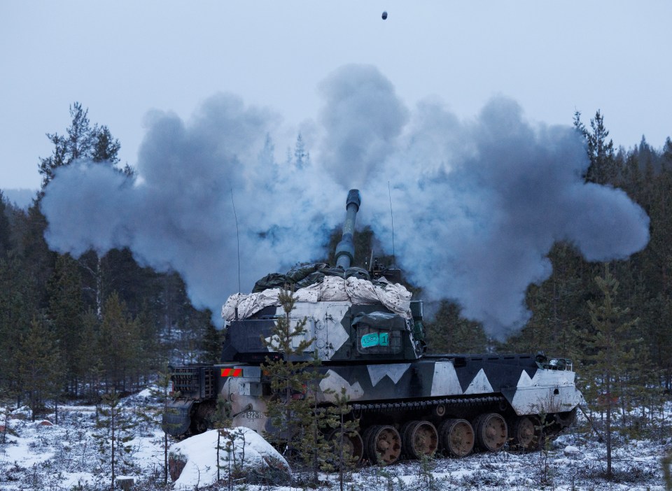 A camouflaged self-propelled howitzer firing in a snowy forest.